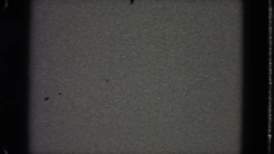 1963 8mm frame showing gray television-style static with visible dust marks, film-edge shadowing, and a faint horizontal line.