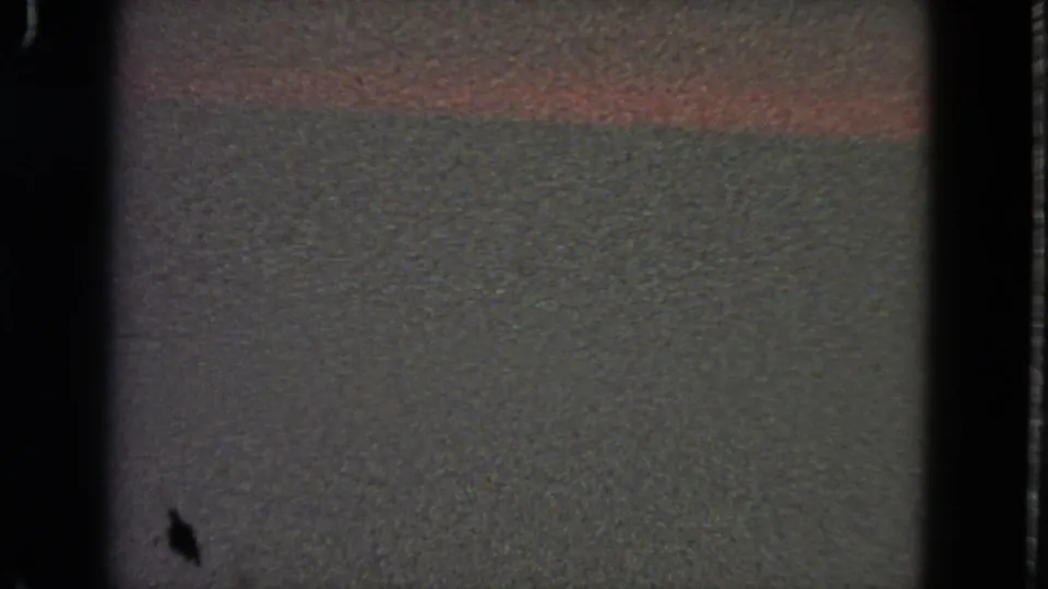 Obstructed 8mm frame with dark borders and a muted surface, likely before the street view becomes clear.