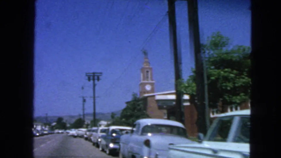 1963 San Francisco street scene showing rows of parked cars, utility poles, trees, and a brick clock tower under clear sky.