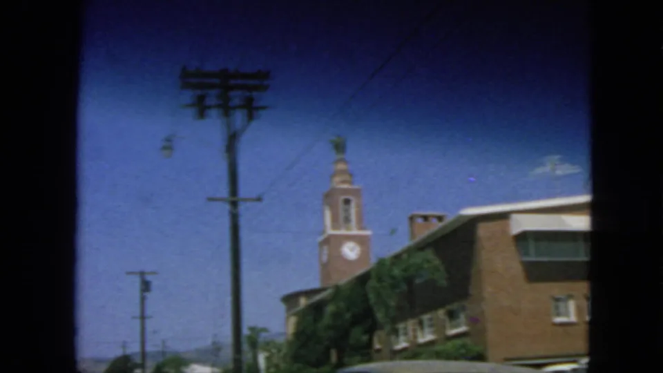 Handheld 1963 San Francisco street frame with a utility pole foregrounding a brick building and clock tower.