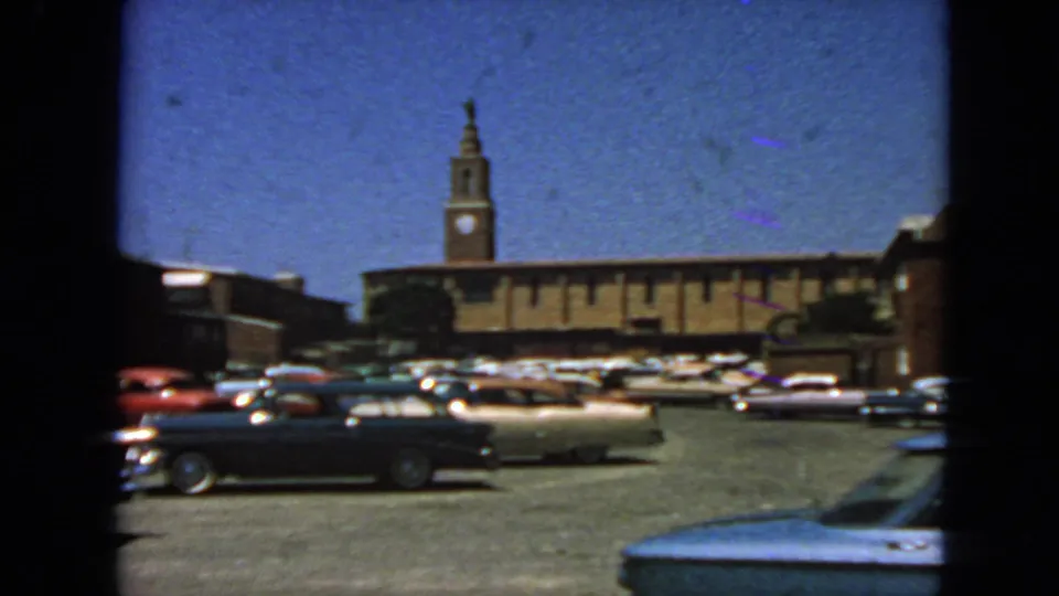1963 San Francisco view of a parking lot with mid-century cars and a long brick building topped by a clock tower.