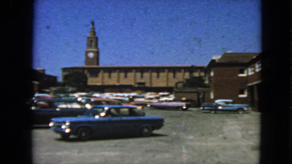 1963 San Francisco home-movie frame showing parked early-1960s cars before a brick building with a clock tower.