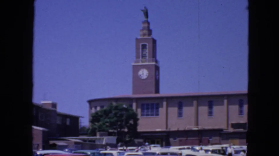 1963 San Francisco 8mm frame showing the clock tower and statue above a low brick building and parked cars.