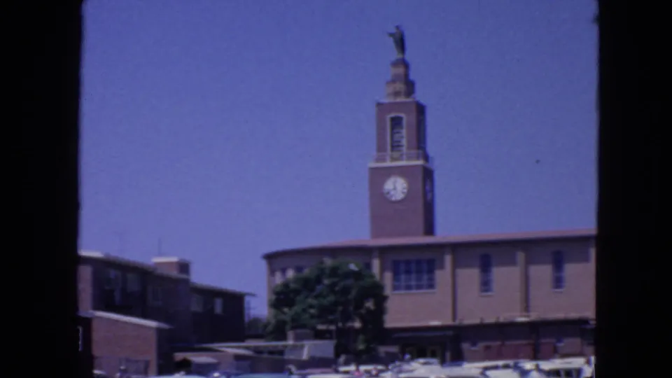 1963 San Francisco 8mm frame showing a church-like clock tower topped by a religious statue, with parked cars below.