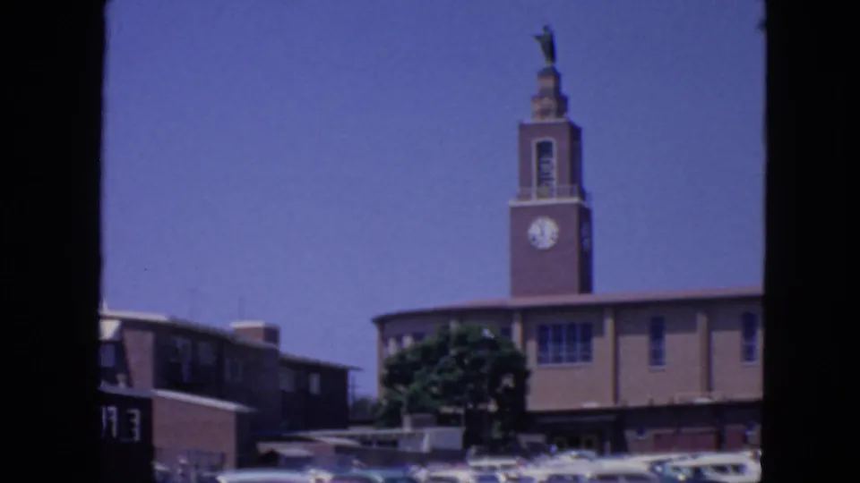 Wide 8mm view of a San Francisco religious tower with a clock face, statue, blue sky, and cars along the street.