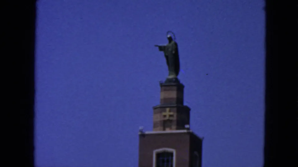 Final 8mm frame focuses on the statue and upper tower, with the figure silhouetted against the San Francisco sky.