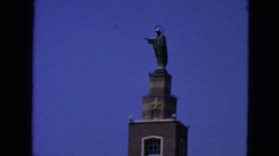 1963 San Francisco frame of the tower-top statue and cross, bordered by dark 8mm film edges.