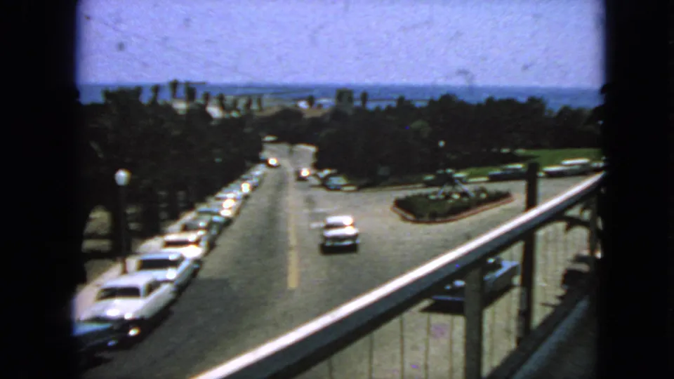 Final 1963 San Francisco home-movie frame showing traffic from above, with a balcony rail, parked cars, trees, and bay view beyond.