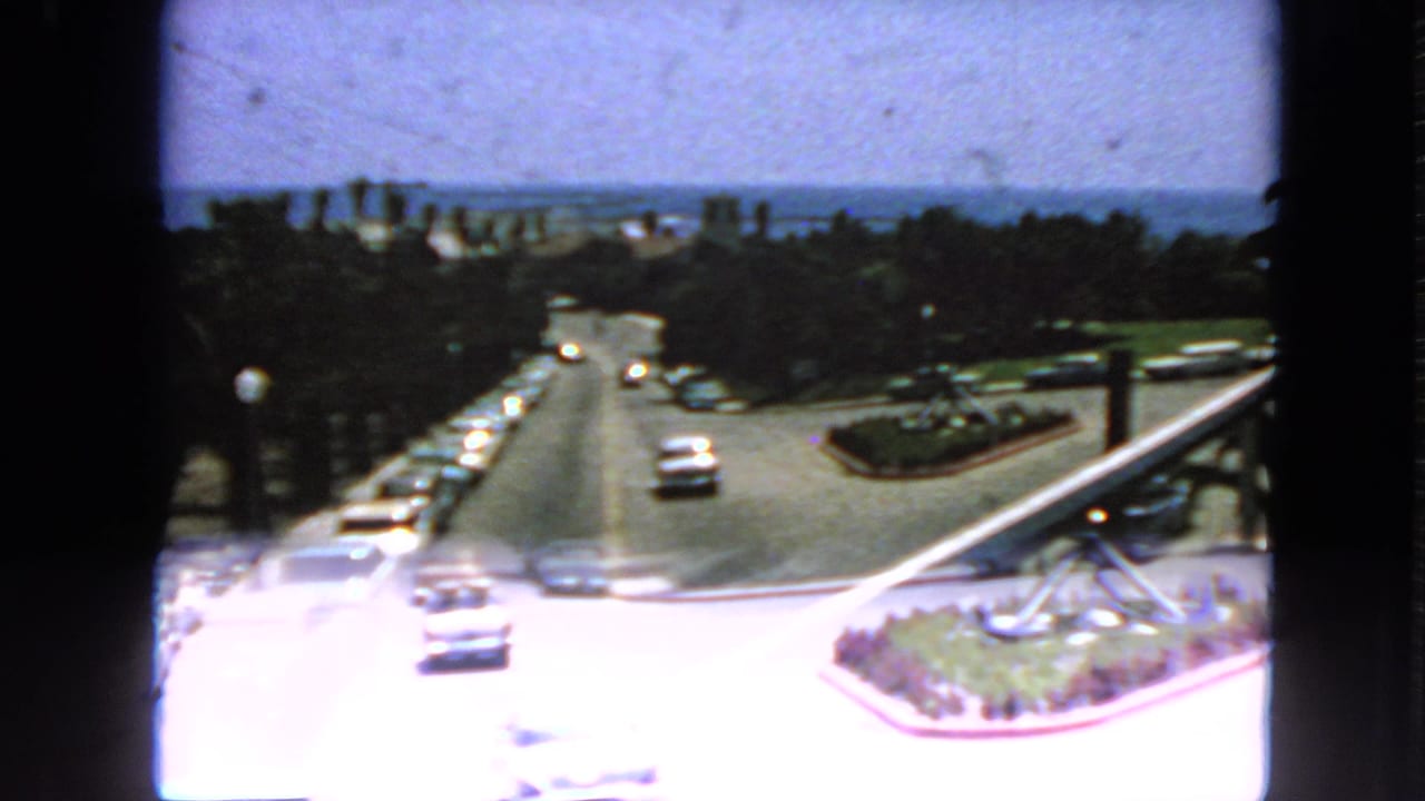 Soft 8mm frame of cars on a sunlit coastal road viewed through dark window edges.