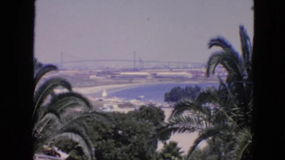 1963 San Francisco 8mm frame with a steady overlook view of water, shoreline, palm foliage, and a distant bridge.