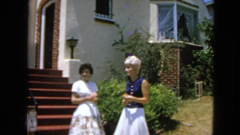 The two women continue down the red-carpeted steps outside a San Francisco residence, with garden shrubs and brick trim behind them.