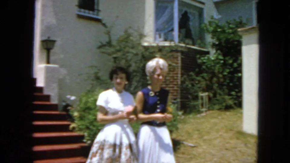 Two adult women pause or walk together near the bottom of exterior steps in 1963 San Francisco, with a residential garden behind them.
