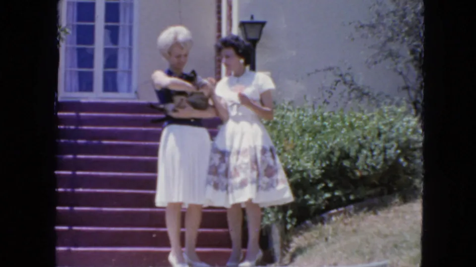 Two women stand near purple-painted steps outside a San Francisco residence in 1963, with one holding a small cat at waist height.