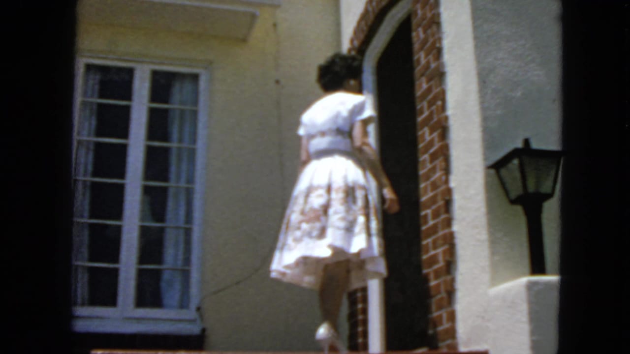 Woman in a light dress approaches an arched brick doorway beside a multi-pane window.