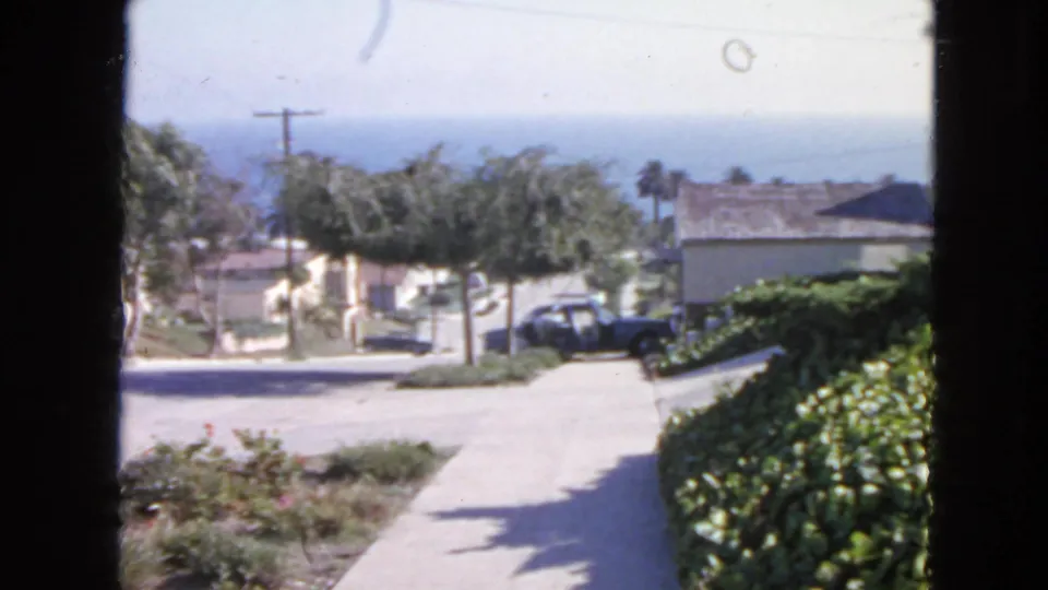 A San Francisco residential street appears beyond the house, with sidewalk, parked cars, trees, low buildings, and ocean in the distance.