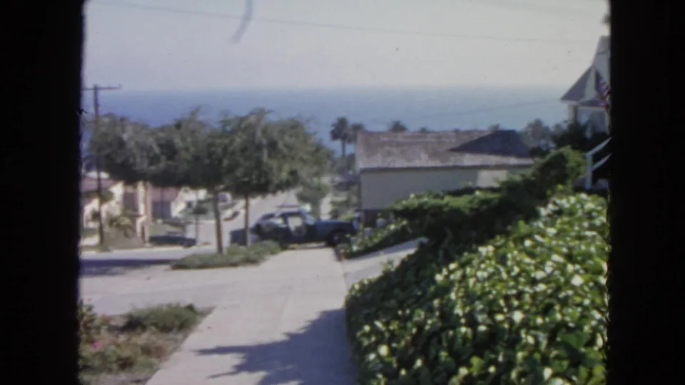 Final 1963 San Francisco frame shows the same window-framed residential street, with hedges, houses, parked car, trees, and ocean beyond.