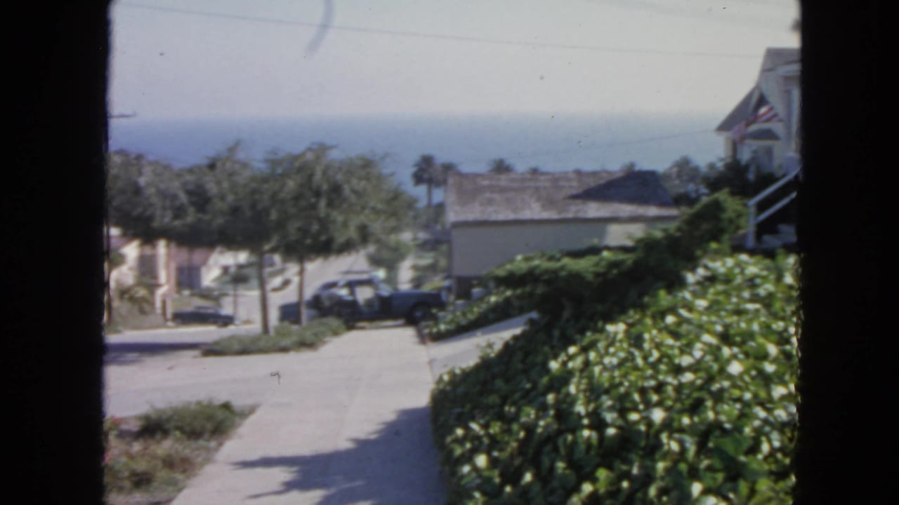 1963 San Francisco home-movie view from a window toward a quiet residential street and distant ocean horizon.