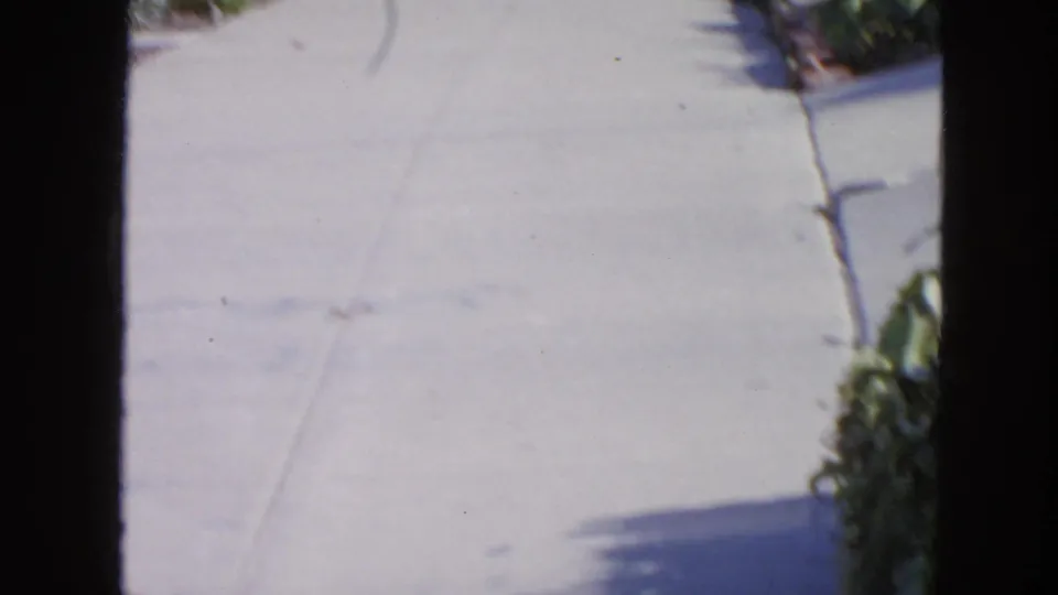 1963 San Francisco home-movie frame showing a quiet residential street and sidewalk, with dark vertical film borders in view.