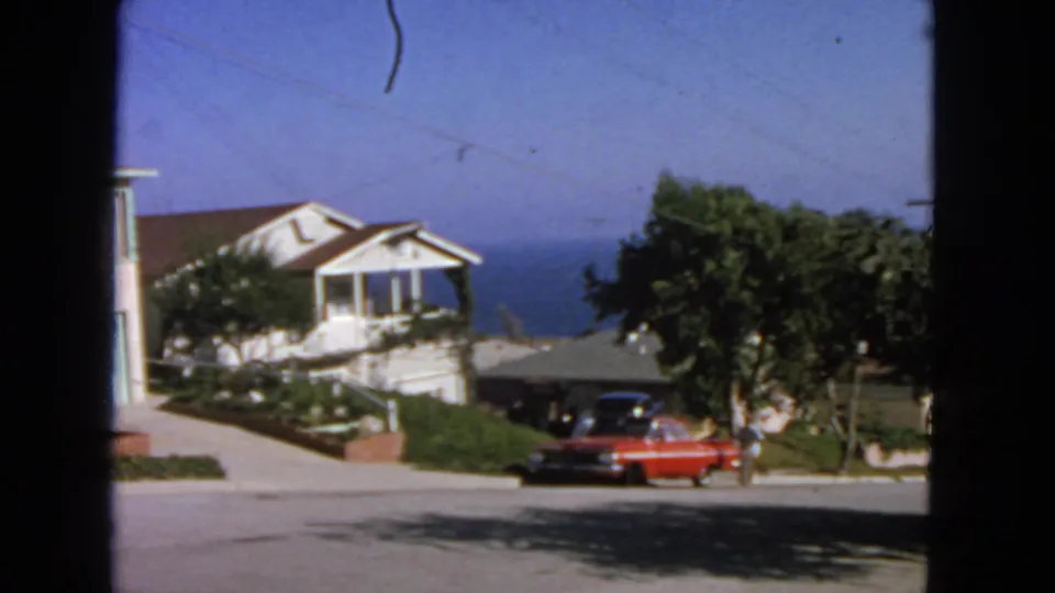 Final 1963 San Francisco frame showing the red sedan at the curb, a small adult figure, nearby homes, trees, and distant water.