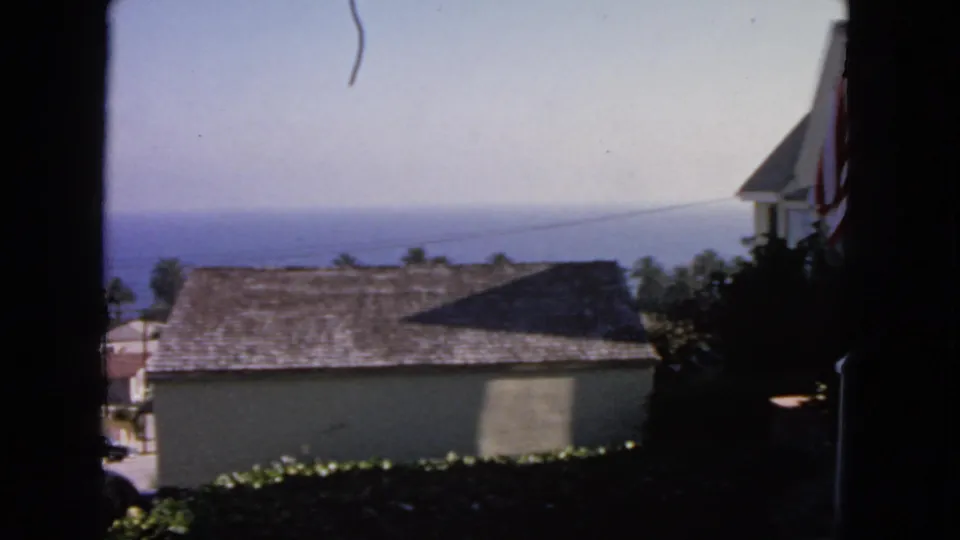 1963 San Francisco coastal view with a shingled roof, partial American flag, vegetation, and distant ocean.