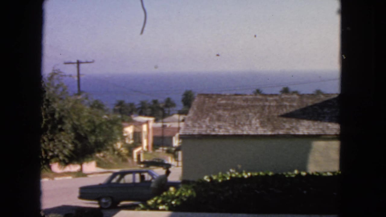 Window-framed view of a sedan parked on a residential street with ocean in the distance.