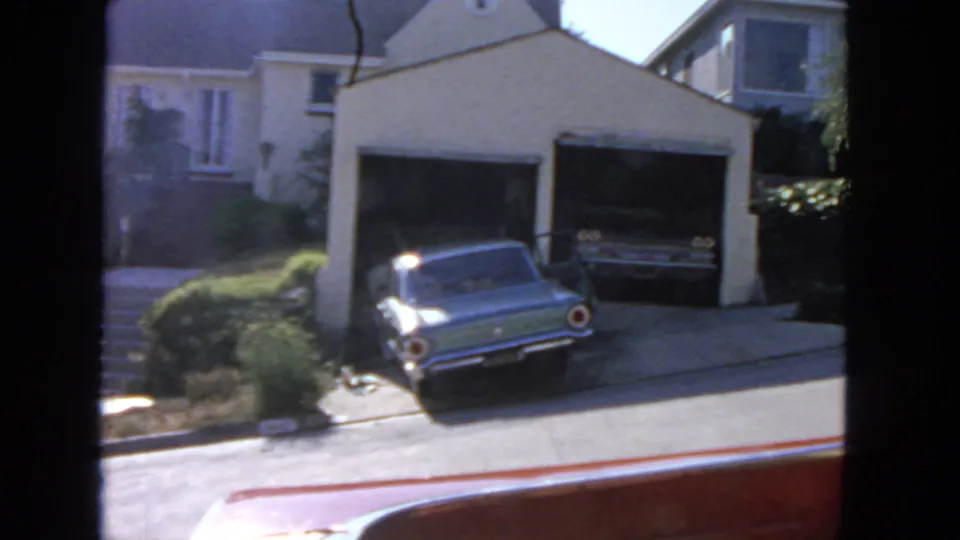 1963 San Francisco residential view with a blue car in the driveway and another car visible inside the garage.