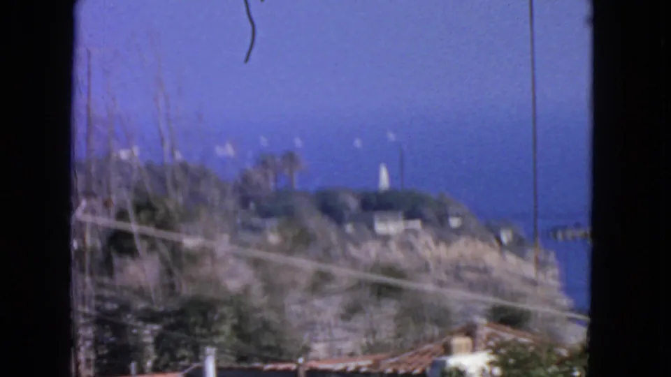 1963 San Francisco coastal view with a brushy hillside, ocean background, utility lines, and a distant white tower or lighthouse.