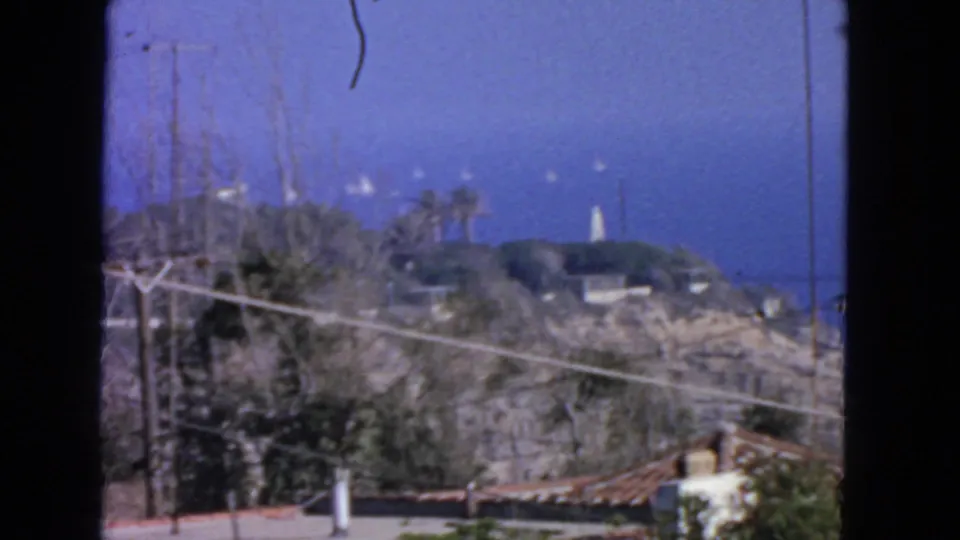 1963 San Francisco home-movie view across a coastal slope toward the ocean and a distant white tower or lighthouse.