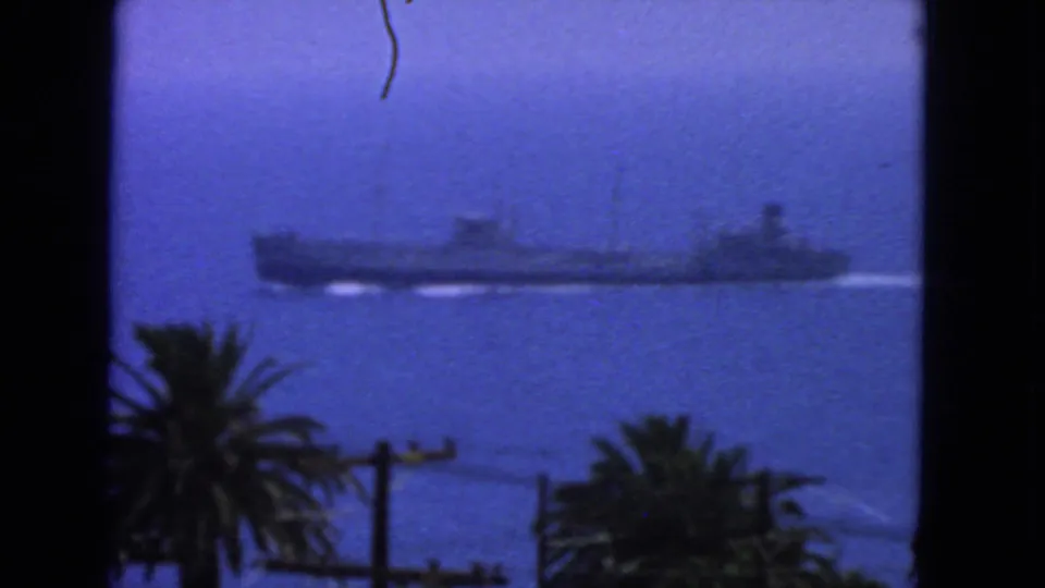 1963 San Francisco shoreline view of a large ship on open water, with palms, utility poles, and soft 8mm color saturation.