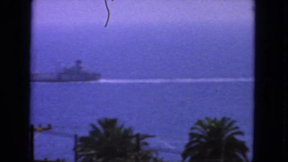 1963 San Francisco coastal frame showing the distant naval vessel near the left edge, with its wake extending across calm blue water.