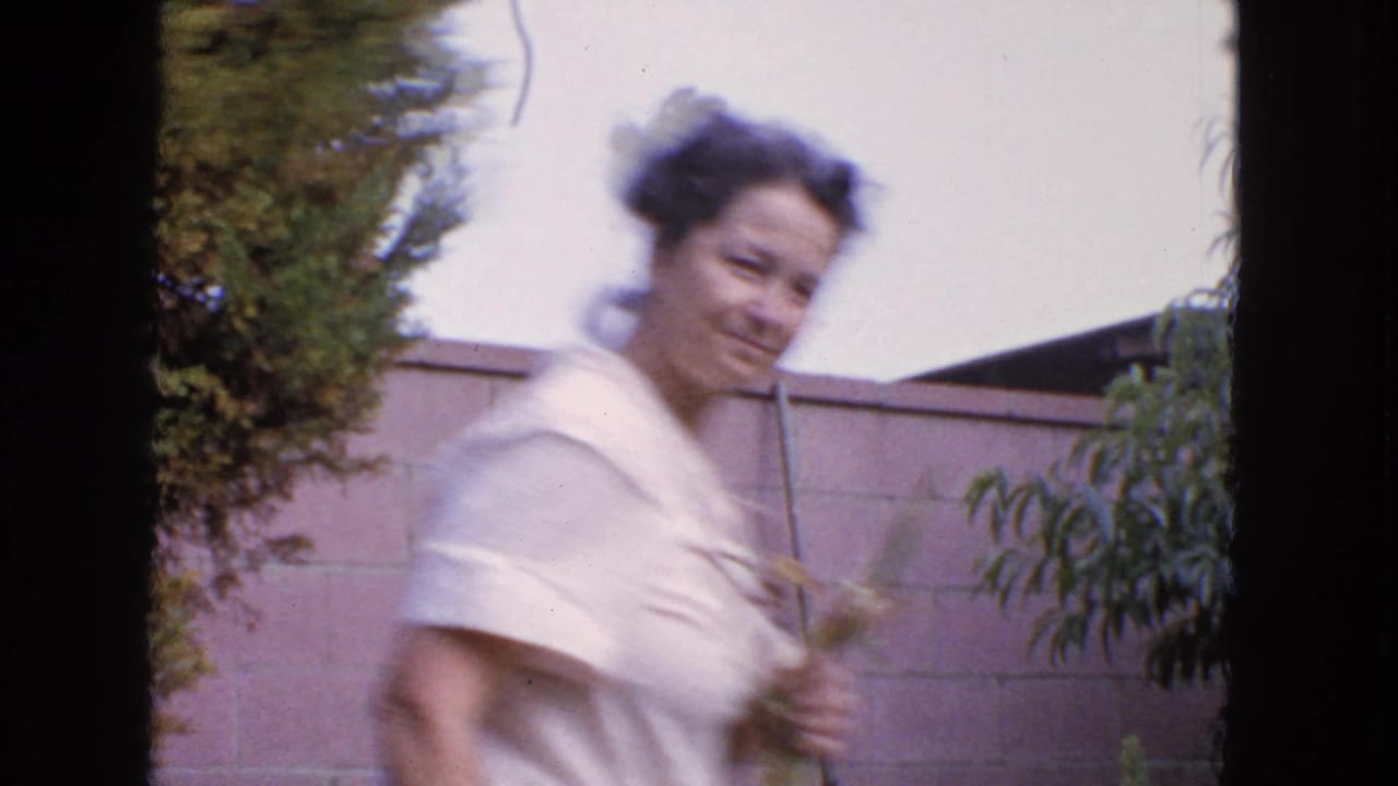 Woman in a light dress walks through a backyard holding plant cuttings.