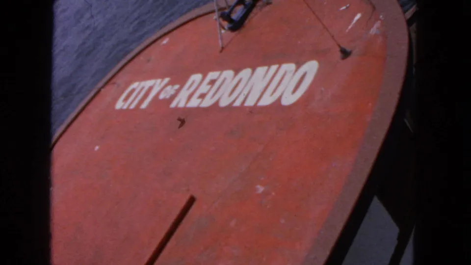 Red circular sign with white letters reading "CITY OF REDONDO," framed close-up with dark film edges and a gray background.