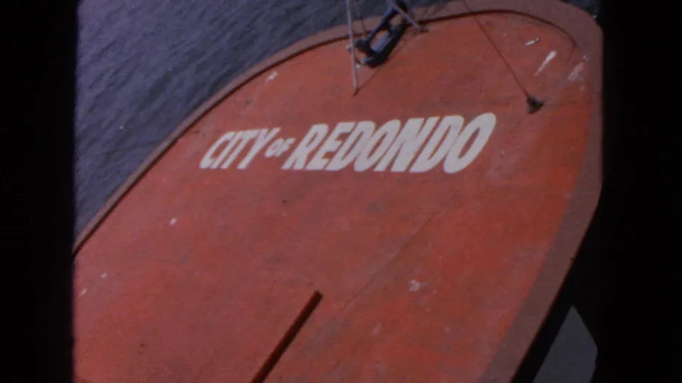 Handheld 8mm close-up of the red "CITY OF REDONDO" sign, showing white lettering, scuffed paint, and partial mounting hardware.