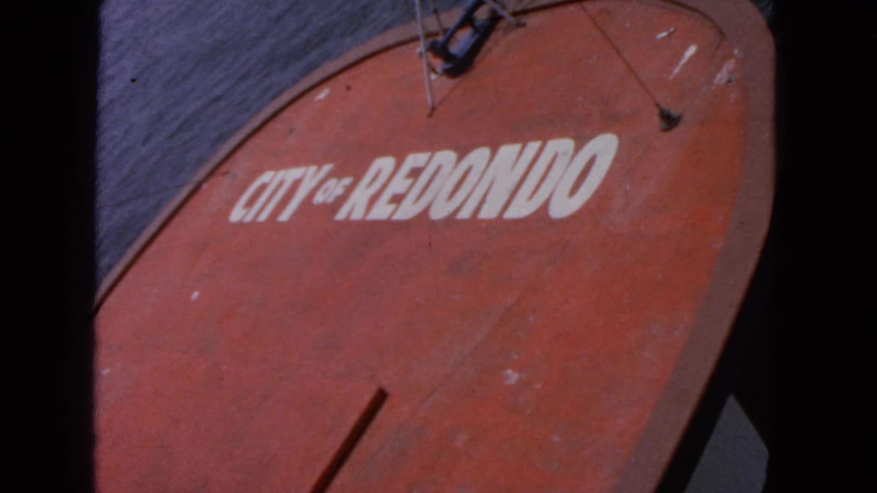Red boat side with white "CITY OF REDONDO" lettering beside dark water.