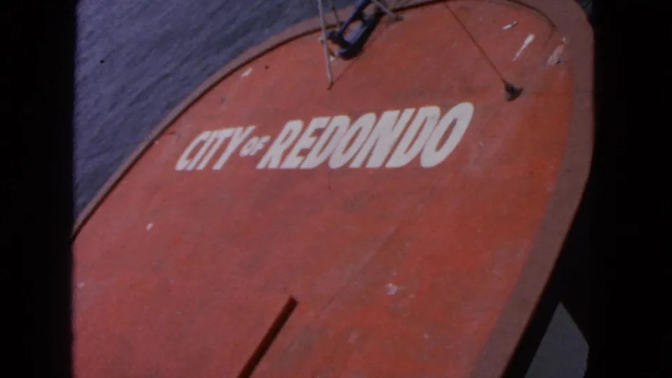 1963 8mm frame showing a close view of a red boat marked "CITY OF REDONDO" on dark water, from the San Francisco clip metadata.