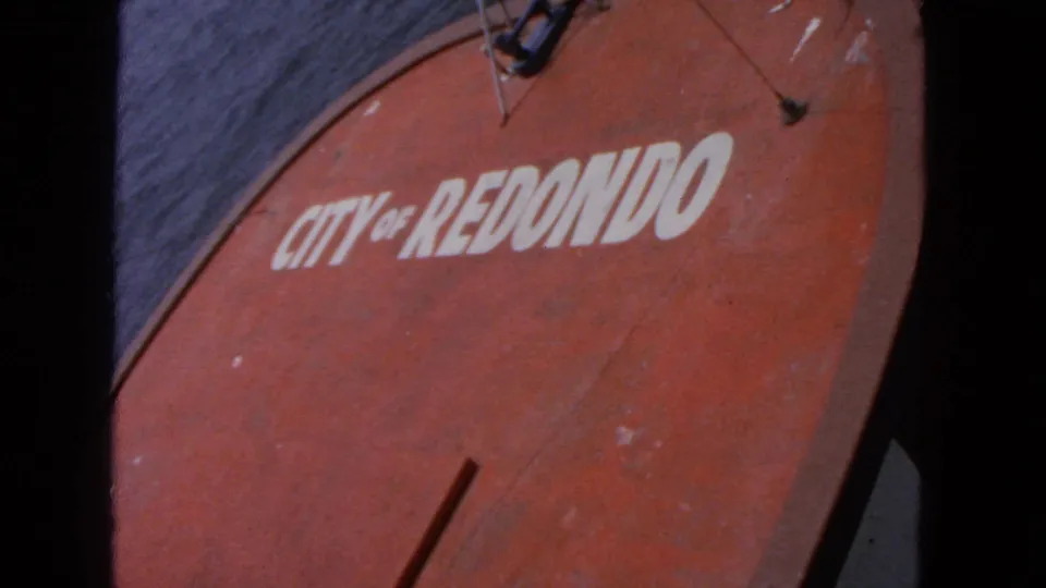 Handheld 1963 home-movie frame of the red boat marking, with the white lettering and surrounding worn paint filling most of the view.