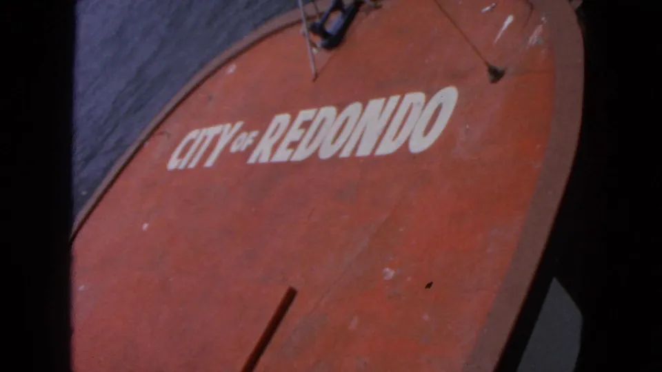 Final 8mm frame holds on the red "CITY OF REDONDO" boat side, with dark water and black film borders around the close composition.