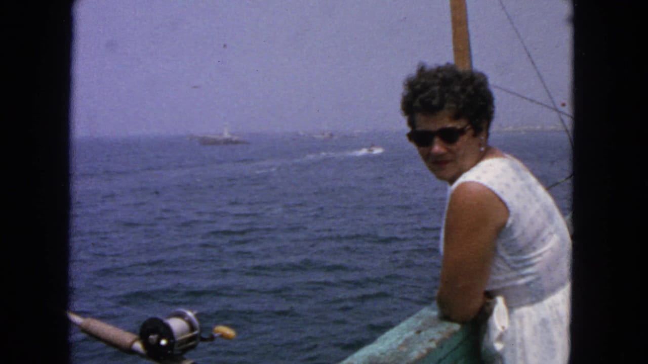 Woman in sunglasses leans on a boat railing beside a fishing rod on open water.