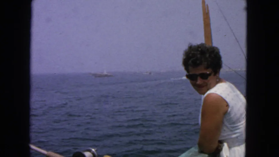 1963 San Francisco-area 8mm frame showing a woman on a boat near fishing gear, with open water and distant vessels in the background.
