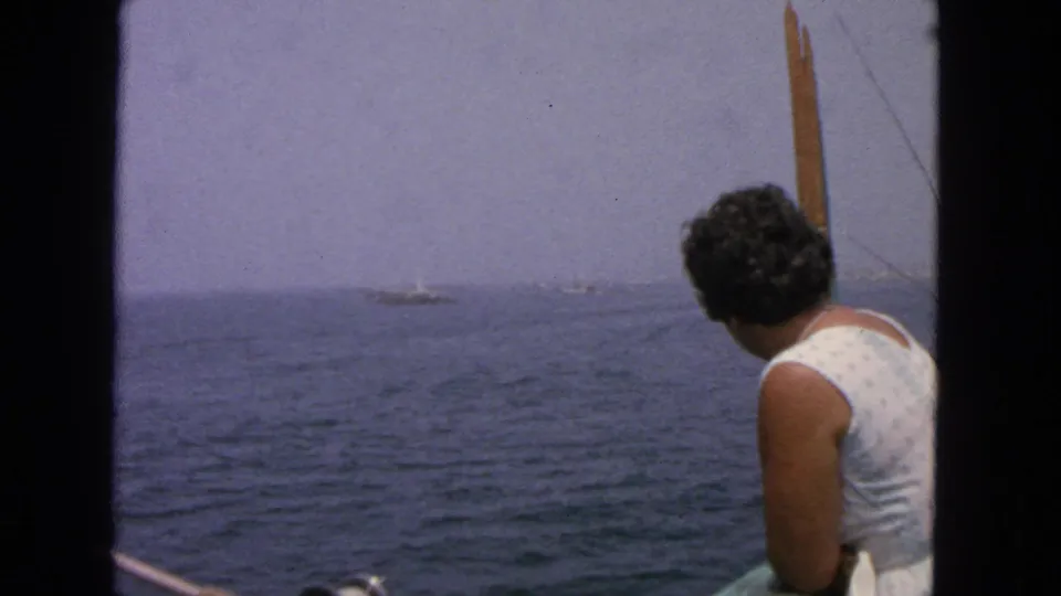 The woman turns away from the camera toward the ocean, with distant boats visible through the soft 8mm haze.