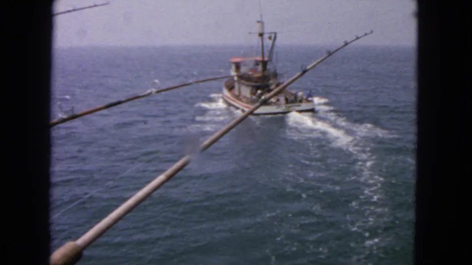 Final 1963 8mm frame of the City of San Francisco fishing boat moving away on open water, with people on deck, rods in the foreground, and dark film borders visible.