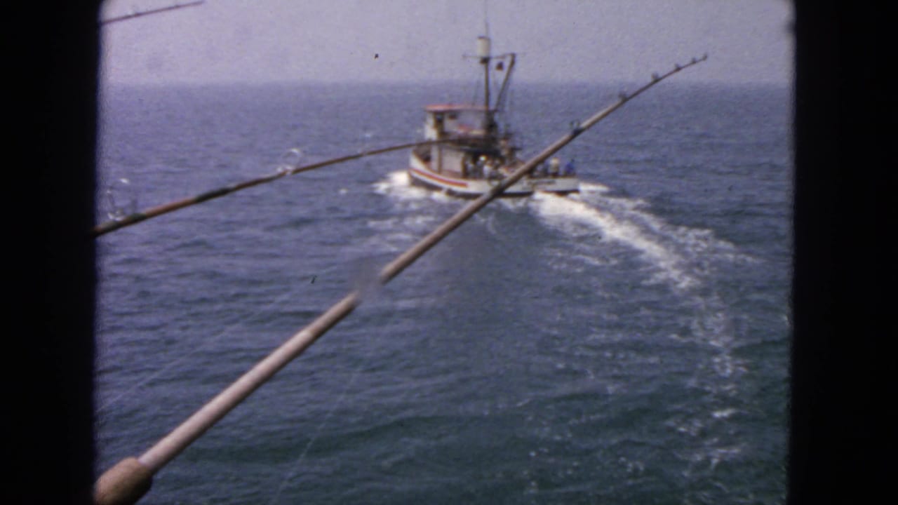 Small boat passing on open water with fishing rods crossing the foreground.