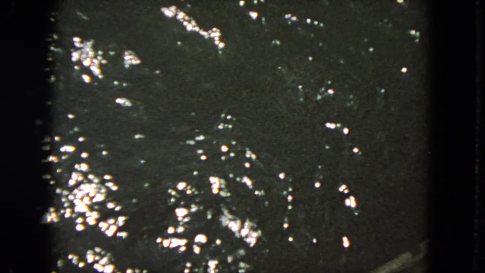A close home-movie view of reflective bay water closes the clip, with grain, soft exposure, and dark frame edges.