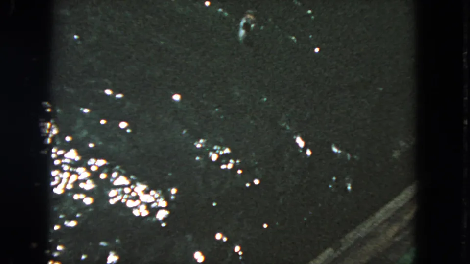 1963 San Francisco 8mm frame showing dark water, scattered reflections, and a small fish-like shape near the surface.