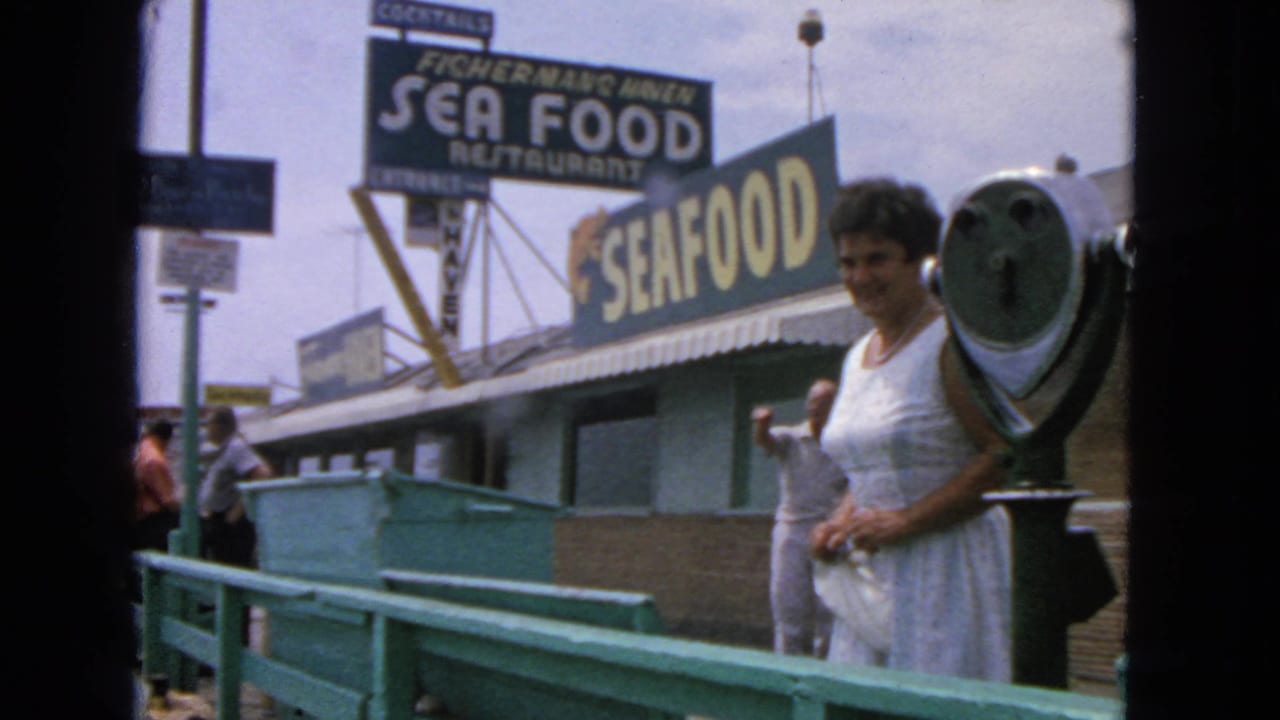 Woman stands near a metal viewer with seafood signs and pedestrians visible behind her.