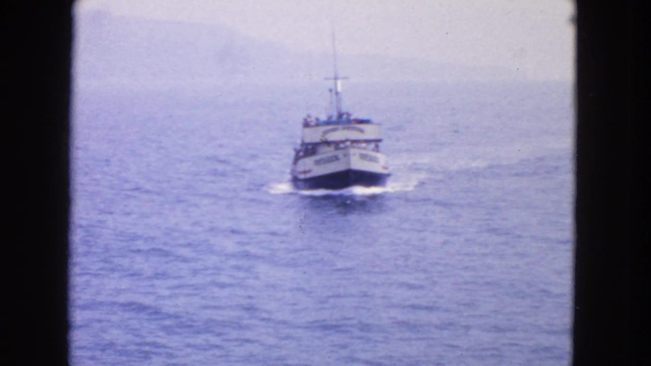 White passenger boat approaches across blue water with a hazy shoreline behind it.
