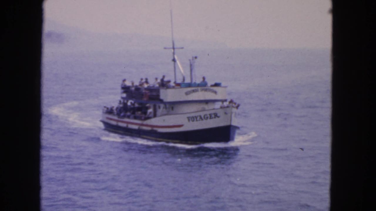 The white-and-red Voyager passenger boat approaches across open water, with a crowded upper deck visible in the 1963 footage.