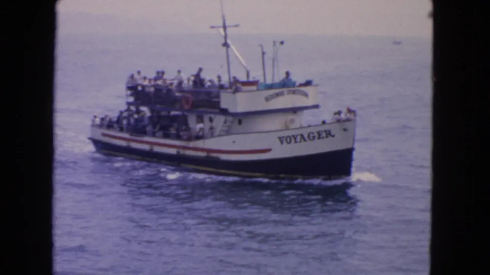 Close 8mm frame of the Voyager boat, its name readable on the hull as passengers ride on the upper and lower decks.