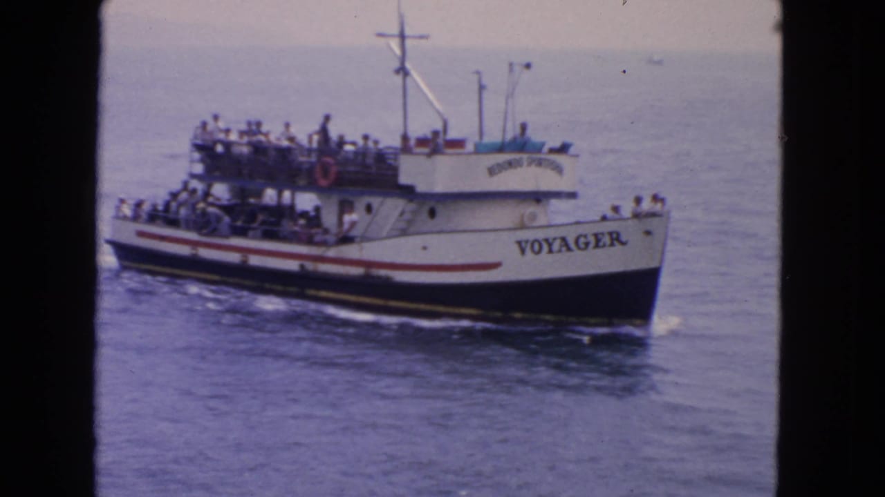1963 San Francisco home-movie frame showing the white passenger boat Voyager moving across calm water with passengers on deck.