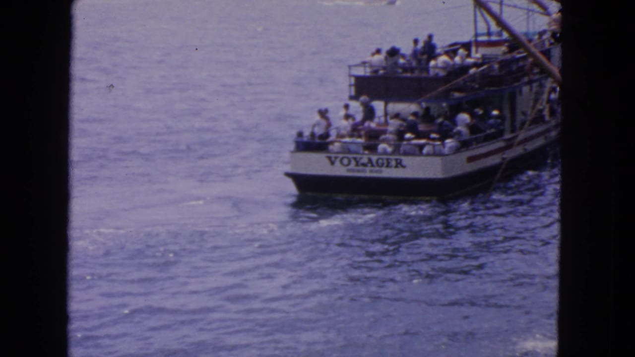 Crowded tour boat named VOYAGER moving across calm water.